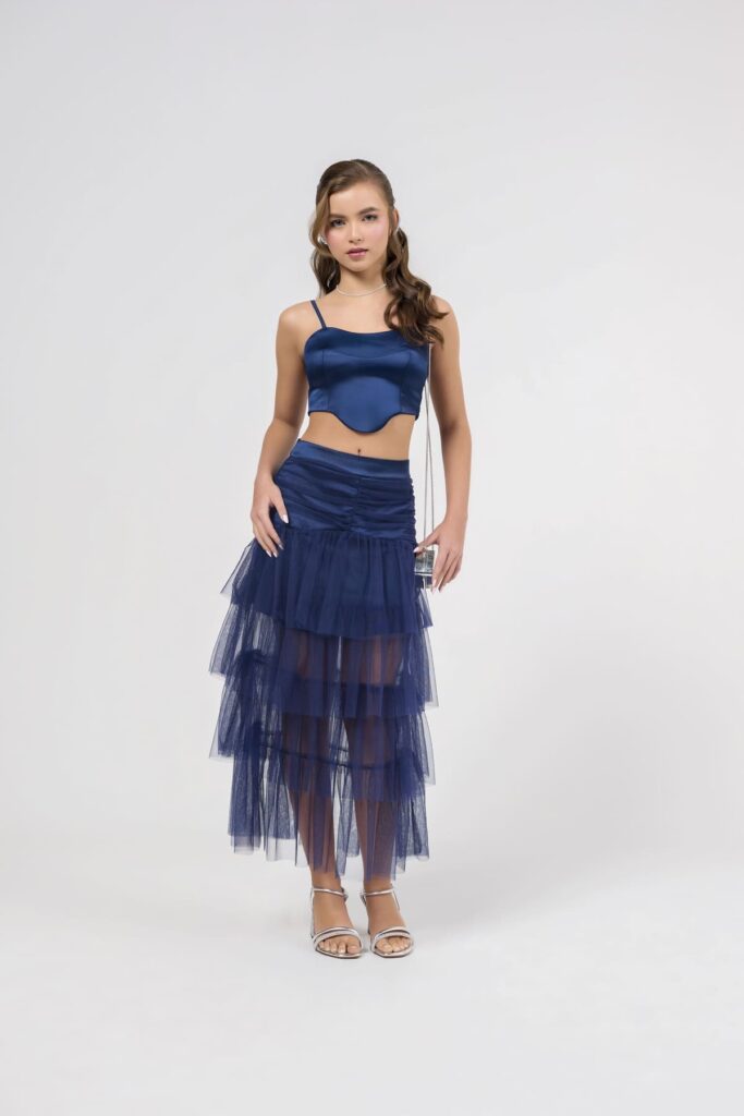 Modelo Adolescente veste um look azul royal estiloso com cropped de alças ajustáveis e uma saia com um tule sobreposto longo sobreposto dando charme para ocasiões especiais.